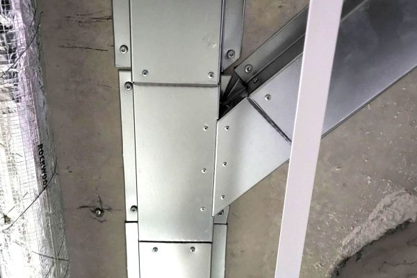 Metallisches Y-Stück einer Leitungsführung an einer Betonwand neben einer isolierten Rohrleitung montiert.