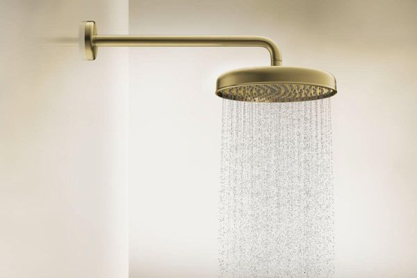 AXOR Archivio Kopfbrause in Goldoptik mit fließendem Wasserstrahl an einer hellen Wand montiert.