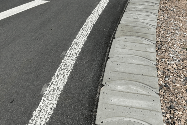 Bankettplatten aus Beton sichern die Fahrbahnränder einer asphaltierten Straße im professionellen Straßenbau.