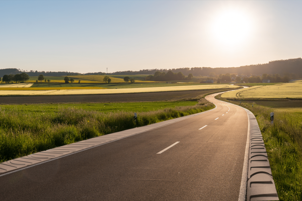 EHL Bankettplatte zur Befestigung einer kurvigen Landstraße durch Felder bei tiefstehender Sonne.