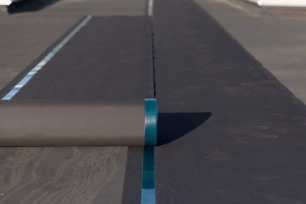 Zwei schwarze EPDM-Abdichtungsbahnen werden fachgerecht nebeneinander auf einem Flachdach verlegt.