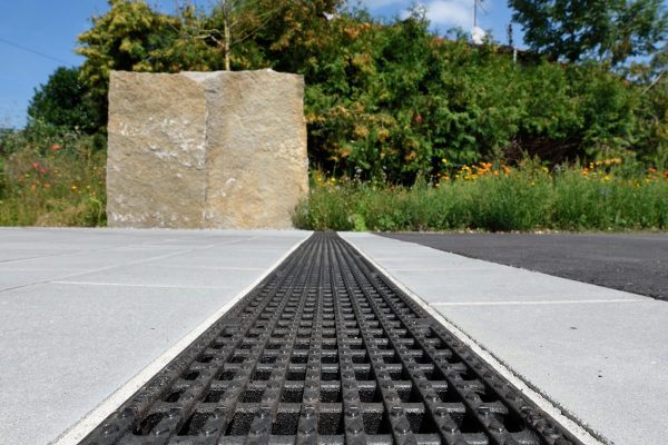 ACO DRAIN Multiline Seal in Entwässerungsrinne mit schwarzem Gussrost auf Pflasterfläche für Grundwasserschutz.
