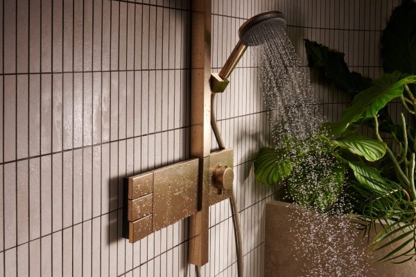 Ein neuer Archetyp eines Aufputzthermostats in Bronze mit fließendem Wasser vor hellen Fliesen und Pflanzen