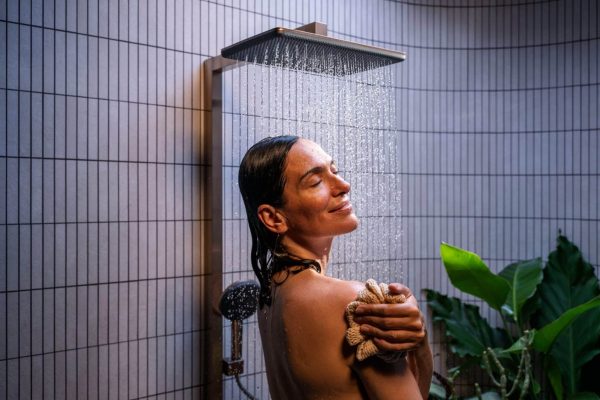 Frau unter einer Regendusche mit modernen Armaturen für nachhaltiges Wassersparen kombiniert mit Duschfreude.