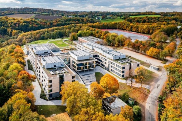 Zukunftsweisende Architektur der Gesamtschule am Waldschlösschen aus der Vogelperspektive inmitten herbstlicher Wälder.
