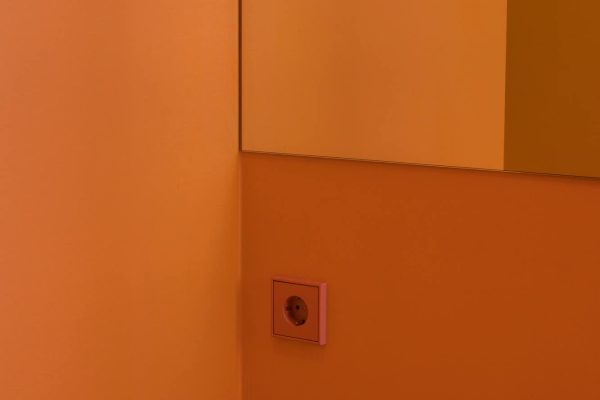 JUNG SCHUKO Steckdose LS 990 in kräftigem Orange Vif auf einer farblich abgestimmten Wand im modernen Design.