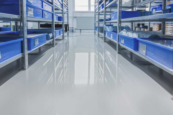 Hellgrauer ESD-Boden in einer Produktionshalle mit blauen Lagerkisten für sichere und sensible Produktionsprozesse.