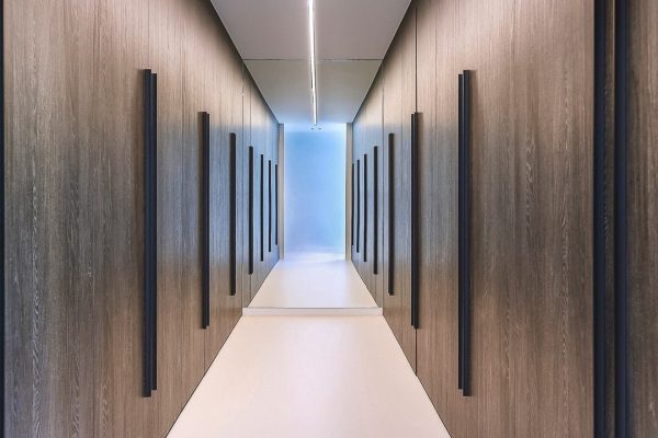 Heller emissionsarmer Designboden in einer puristischen Flurzone mit dunklen, wandhohen Einbaumöbeln.