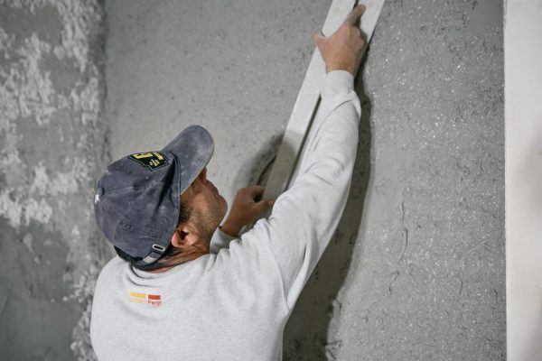 Handwerker beim Klimasan IN glätten an einer Wand mit einer Abziehlatte für eine ebene Oberfläche.