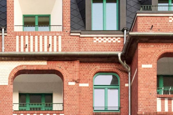 Moderne Aufstockung eines Mehrfamilienhauses in Hamburg mit roter Backsteinfassade und grünen Fenstern.