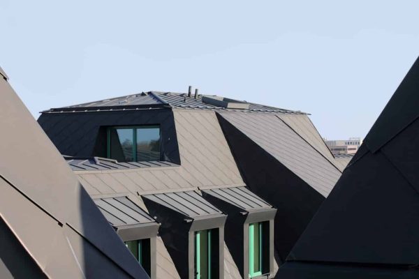 Moderne Aufstockung Mehrfamilienhaus Hamburg mit dunkler Metallverkleidung und markanten Dachgauben vor blauem Himmel.