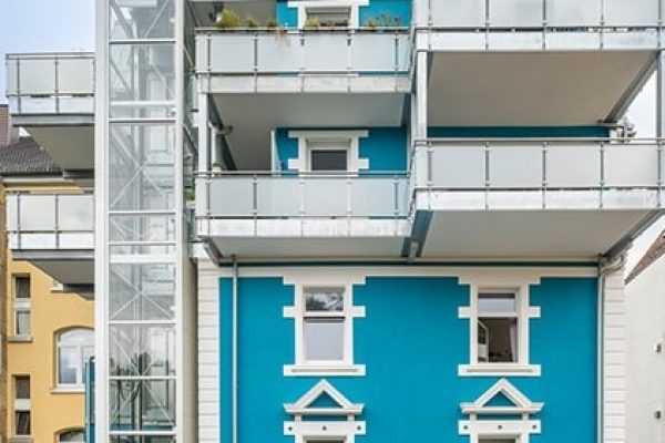Moderner Gen3 Edge Glasaufzug an der blauen Fassade eines Wohnhauses in der Freiburger Habichtsburgstraße 90.