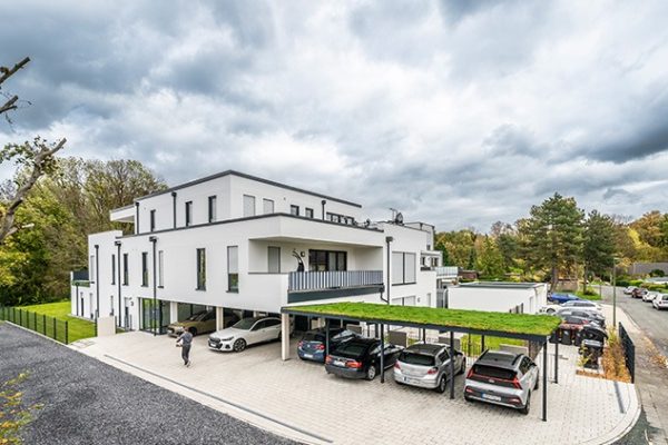 Modernes Mehrfamilienhaus Hamm – Auf dem Döhn 12 Gen360 mit Parkplätzen und begrünten Carports vor bewölktem Himmel.