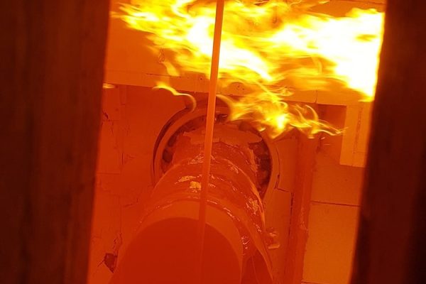 Brandschutztests an einer Rohrdurchführung mit lodernden Flammen in einem speziellen Prüfofen.