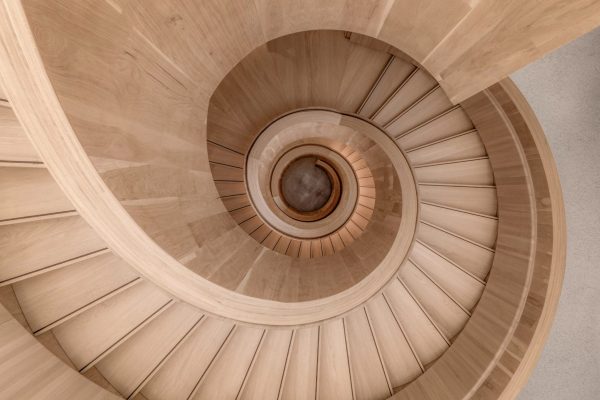 Blick von oben auf die geschwungene Vollholz-Spiraltreppe im Rapunzel Besucherzentrum Legau aus hellem Holz.