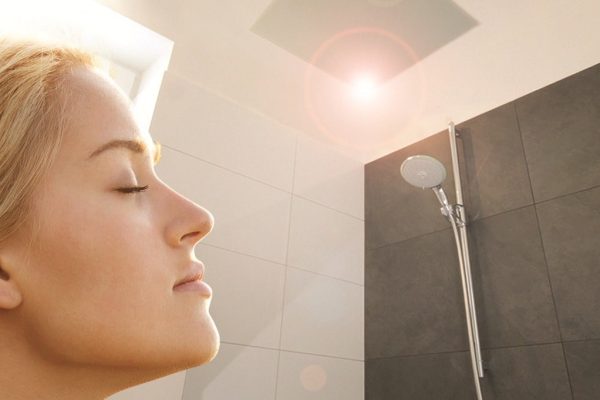 Frau genießt die behagliche Wärme einer Infrarotheizung an der Decke im modern gefliesten Badezimmer.