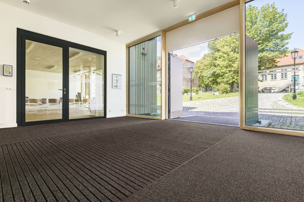 Offener Eingangsbereich mit großflächiger Eingangsmatte und Glasfassade.