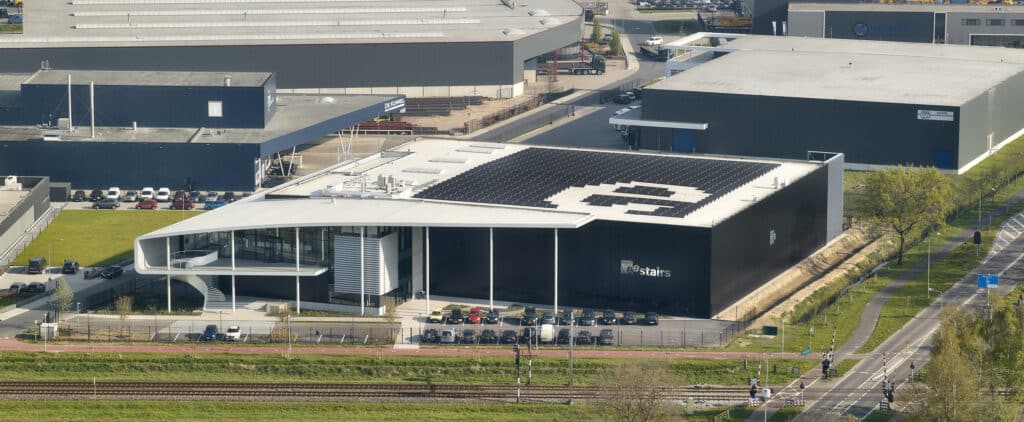 Luftaufnahme eines modernen Firmengebäudes mit großflächiger Solaranlage und futuristischer Fassadengestaltung