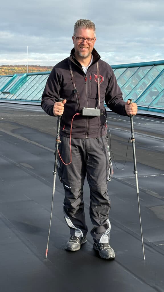 Ein Fachmann steht mit Messgeräten und Sonden auf einem Flachdach, um die Dachabdichtung auf mögliche Leckagen zu überprüfen.