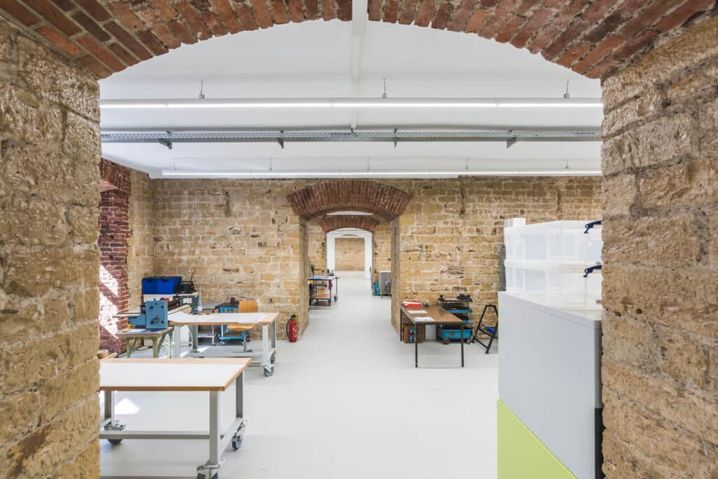 Sanierter Industriebereich mit Sichtmauerwerk, weißen Decken und modernen Arbeitstischen in einem langen, gewölbten Raum.