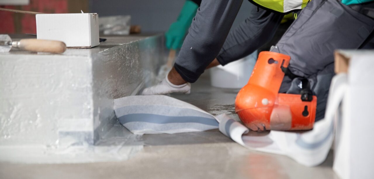 Handwerker bringt Dichtband zur Abdichtung von Bodenanschlüssen in einem Nassbereich an.