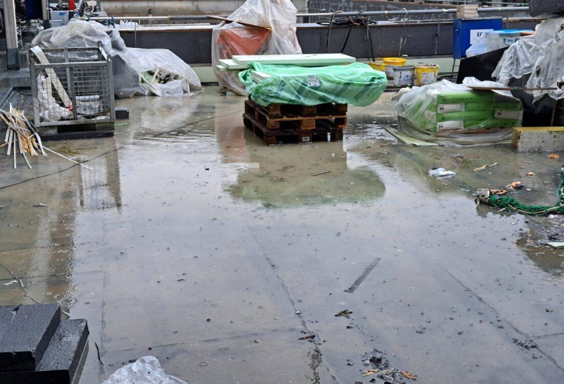 Baumaterialien und Verpackungen auf nasser Dachfläche während der Bauphase.