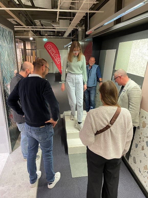 Mehrere Teilnehmende beobachten eine junge Frau, die in einem Showroom einen erhöhten Bodenaufbau testweise begeht.