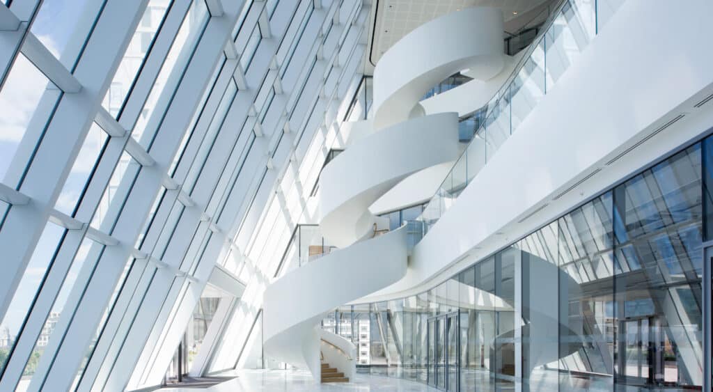 Moderne weiße Wendeltreppe in einem Gebäude mit großflächiger Glasfassade und hellem Atrium