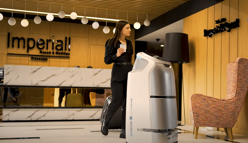 Service-Roboter liefert Getränke im Hotellobby-Bereich, während eine Mitarbeiterin vorbeigeht – moderne Hotelautomation.