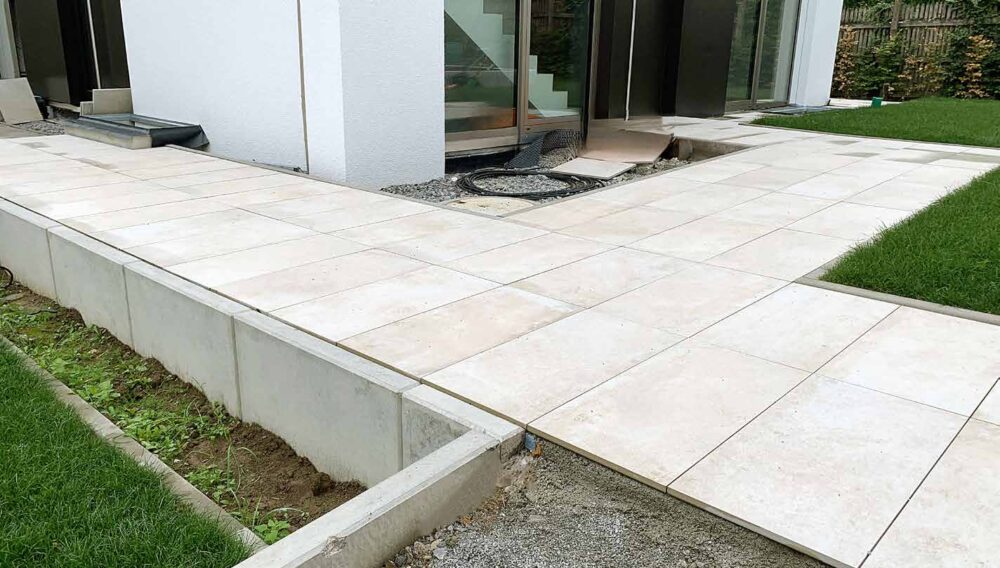 Neu verlegte Terrassenplatten auf Betonunterbau mit angrenzender Grünfläche.