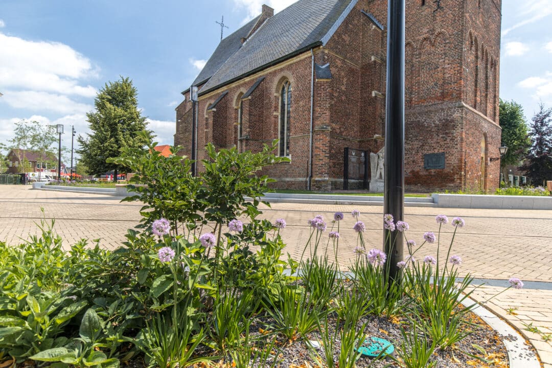 Begrünter Platz mit Pflanzflächen vor einer historischen Kirche im Zentrum von Dinxperlo.