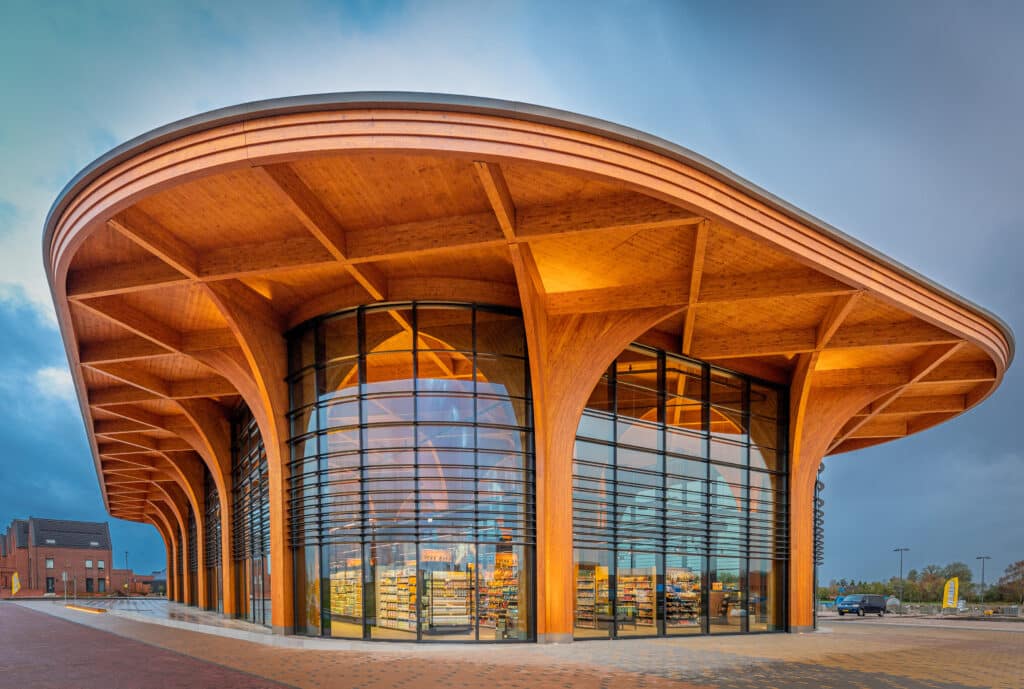 Holzarchitektur mit großen Rundstützen und weit auskragendem Dach des Superhub Meerstad, große Glasfronten und warmes Innenlicht.