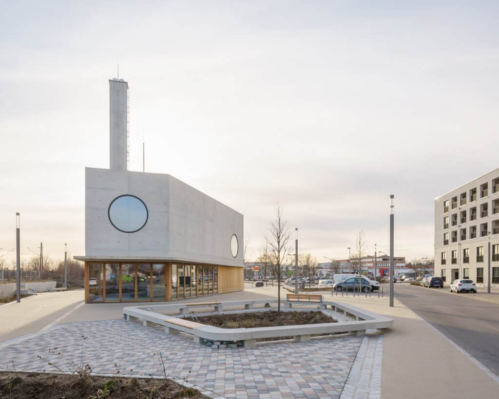 Außenansicht des kompakten Kirchenneubaus mit Betonfassade, kreisrunden Fenstern und Solarlux Glas-Faltwand aus Holzprofilen.