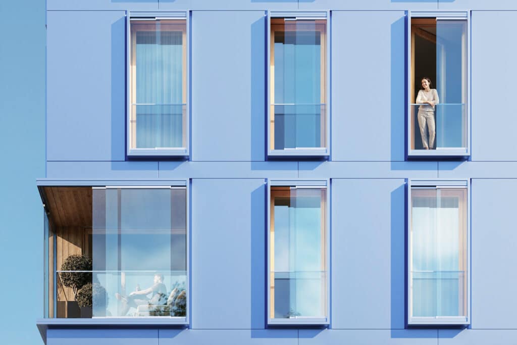 Fassade eines modernen Gebäudes mit schlanken Kastenfenstern von Solarlux; Personen stehen oder sitzen hinter großflächigen Glasfronten, die viel Tageslicht und Transparenz ermöglichen.