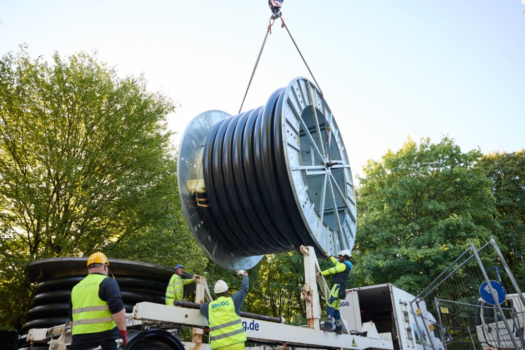 Monteure installieren ein flexibles Rohrsystem von einer großen Kabeltrommel auf einer Baustelle für Energie- oder Versorgungsleitungen.
