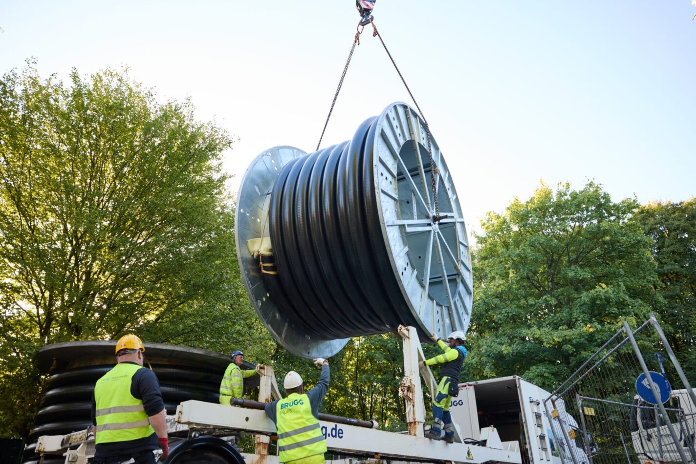 Monteure installieren ein flexibles Rohrsystem von einer großen Kabeltrommel auf einer Baustelle für Energie- oder Versorgungsleitungen.