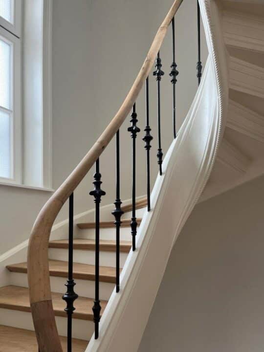 Detail einer geschwungenen Treppe mit Holzhandlauf und schwarzen Stahlstäben im Altbau.