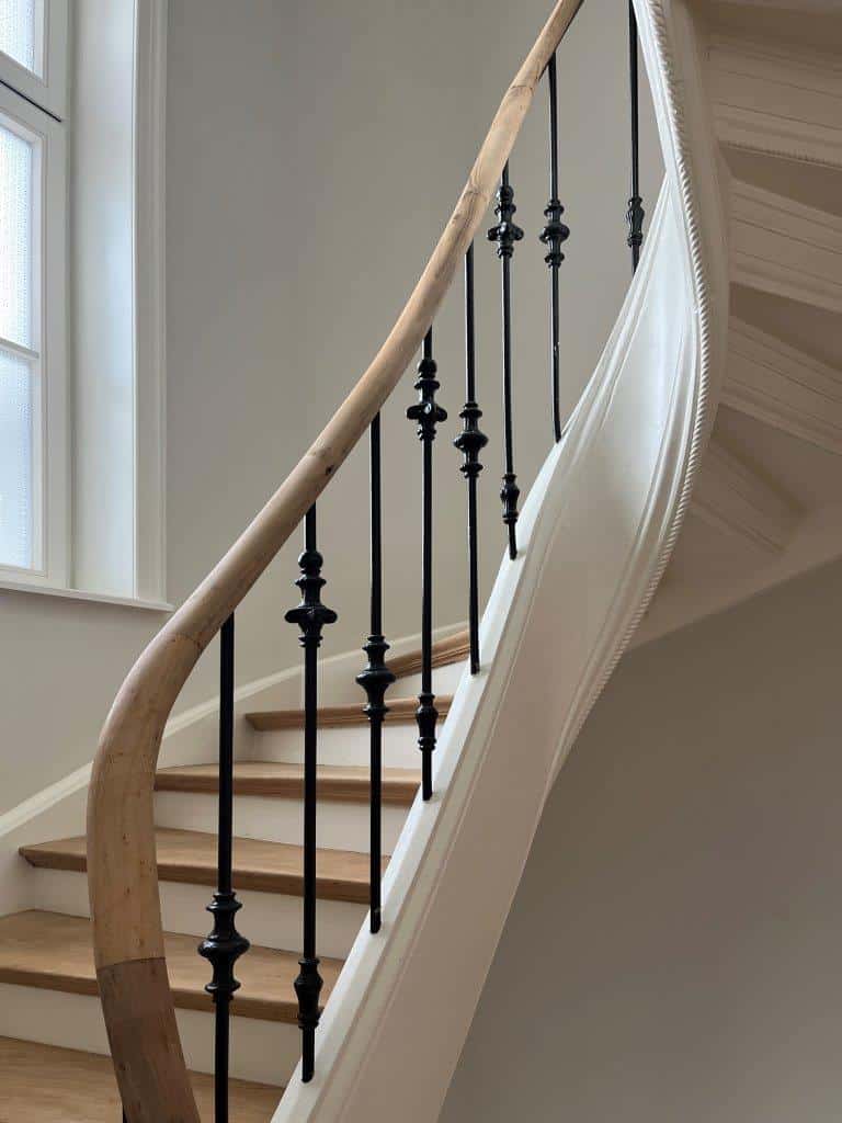 Detail einer geschwungenen Treppe mit Holzhandlauf und schwarzen Stahlstäben im Altbau.