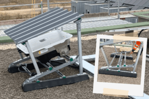 Montierte Wechselrichter-Unterkonstruktion auf einem Kies-Flachdach, bestehend aus einem verzinkten Metallgestell mit Ballastierung; dahinter technische Aufbauten und Dachlandschaft