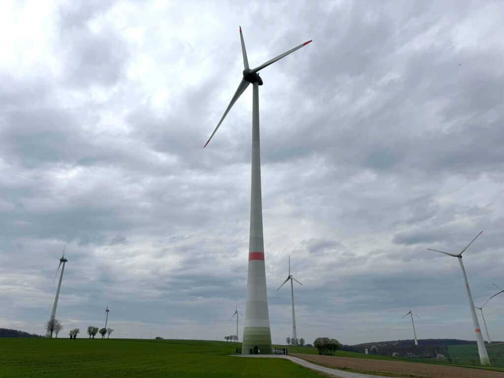 Windkraftanlage in einer grünen Landschaft unter bewölktem Himmel.