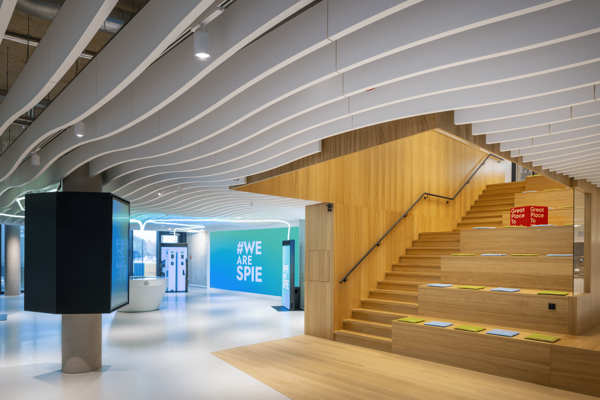 Offenes Bürofoyer mit Holzsitztreppe, moderner Beleuchtung und geschwungener Akustikdecke in einer modernen Unternehmenszentrale.